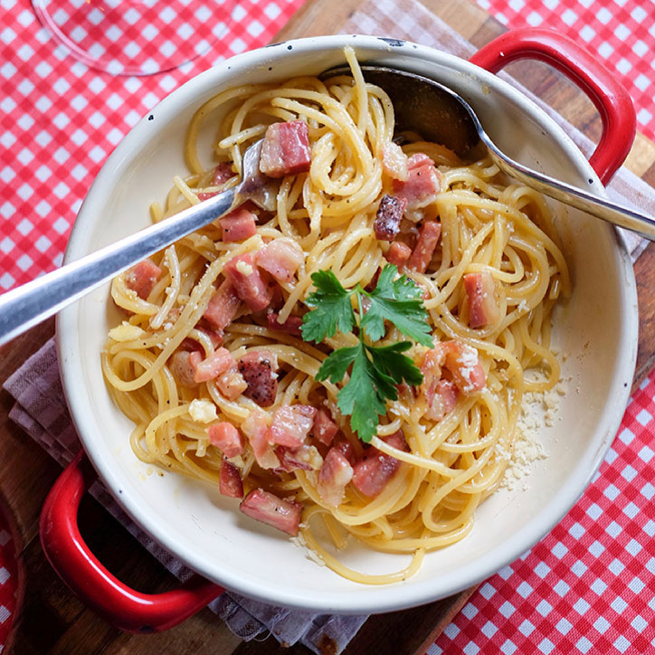 Spaghetti carbonara in a  pot on a table with red and white tablecloth in Rome
